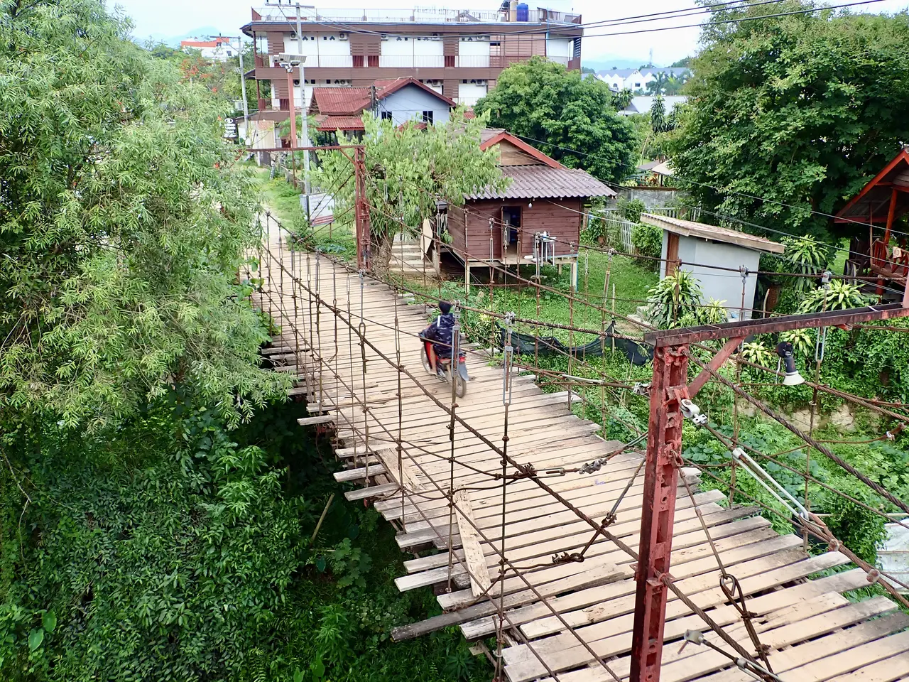 A narrow wooden suspension bridge over the river leading to the quiet side of Vang Vieng