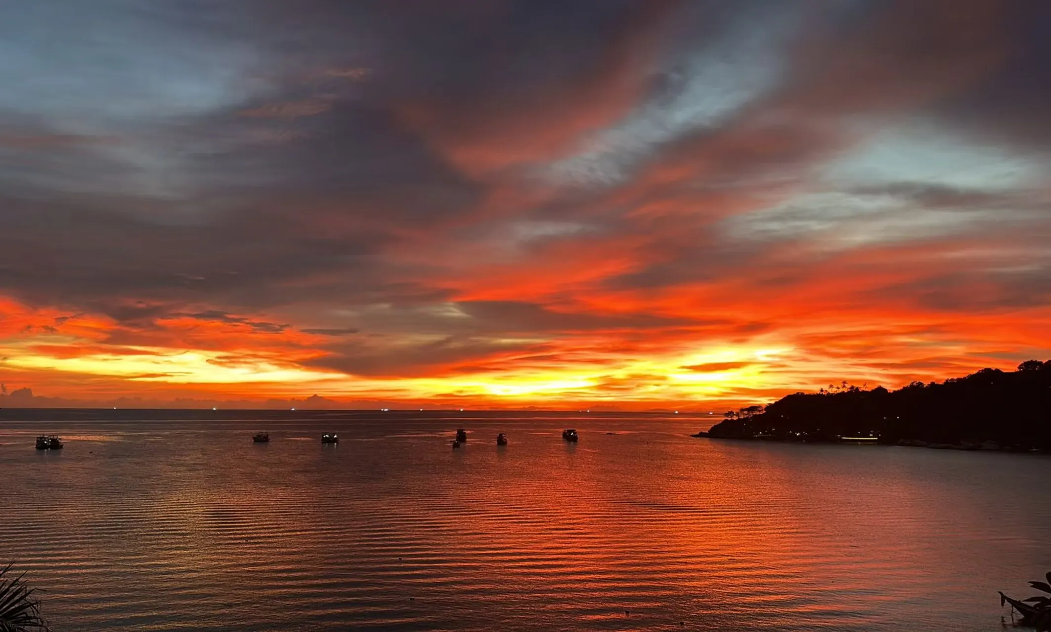 Sunset over the bay in Koh Tao, longtail boats silhouetted on the water