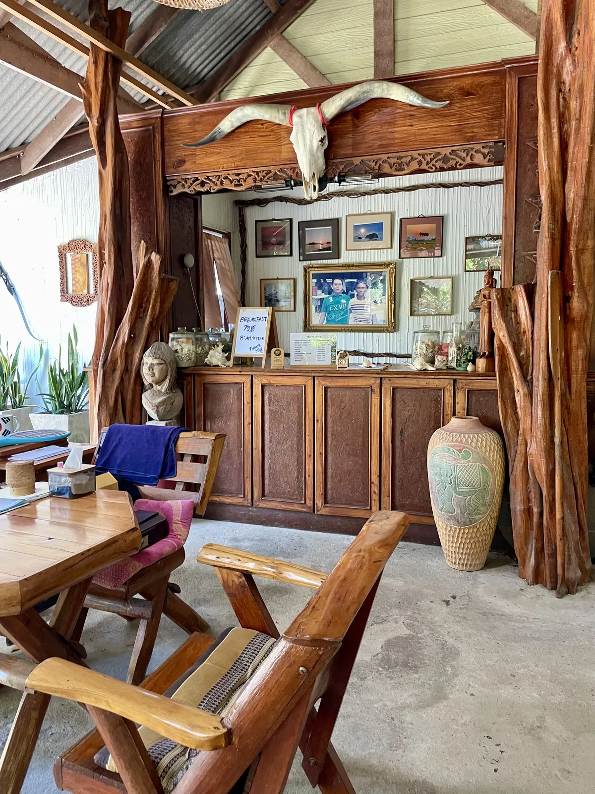 Rustic open-air restaurant interior with carved teak posts, a longhorn skull and framed photos at Dolphin Bay