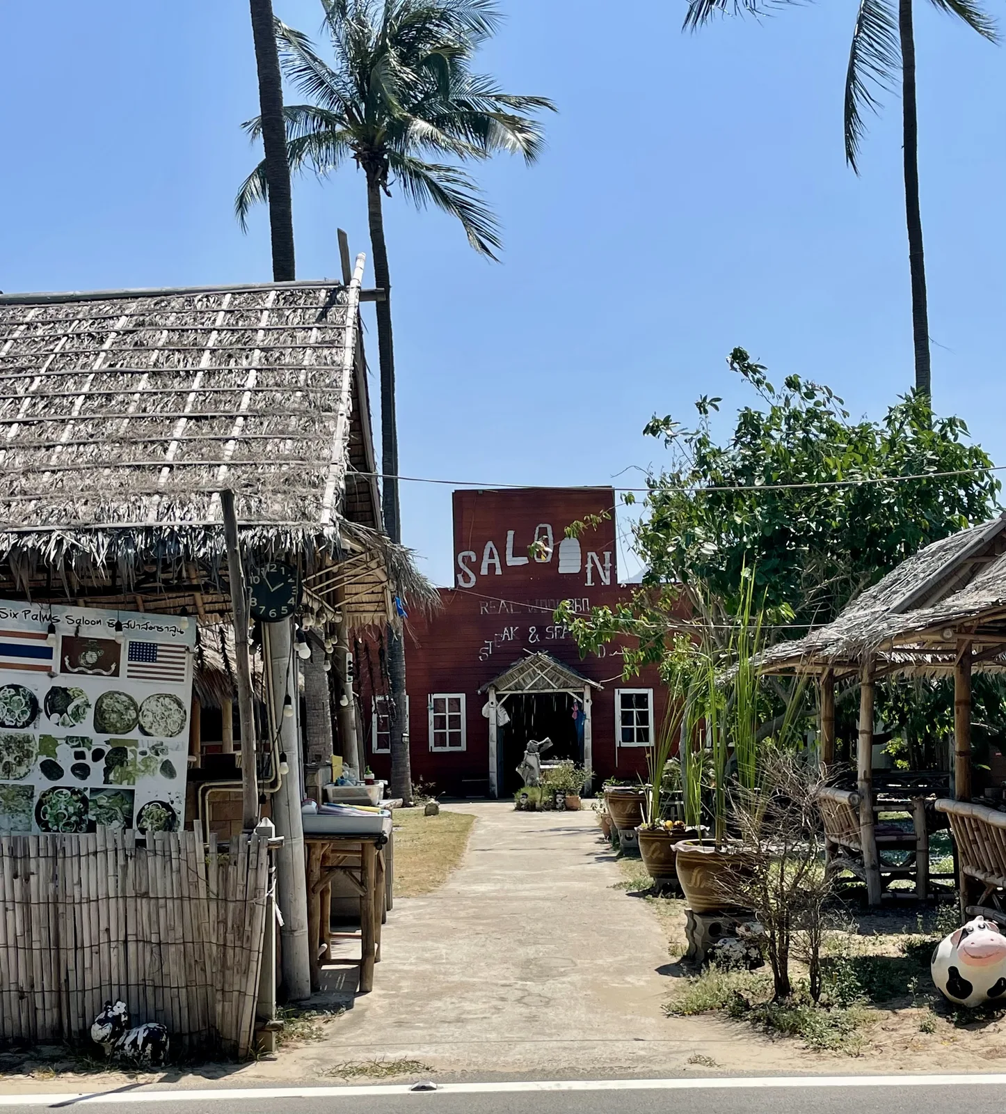 A thatched-roof beachside restaurant called Saloon framed by palm trees at Dolphin Bay, Thailand
