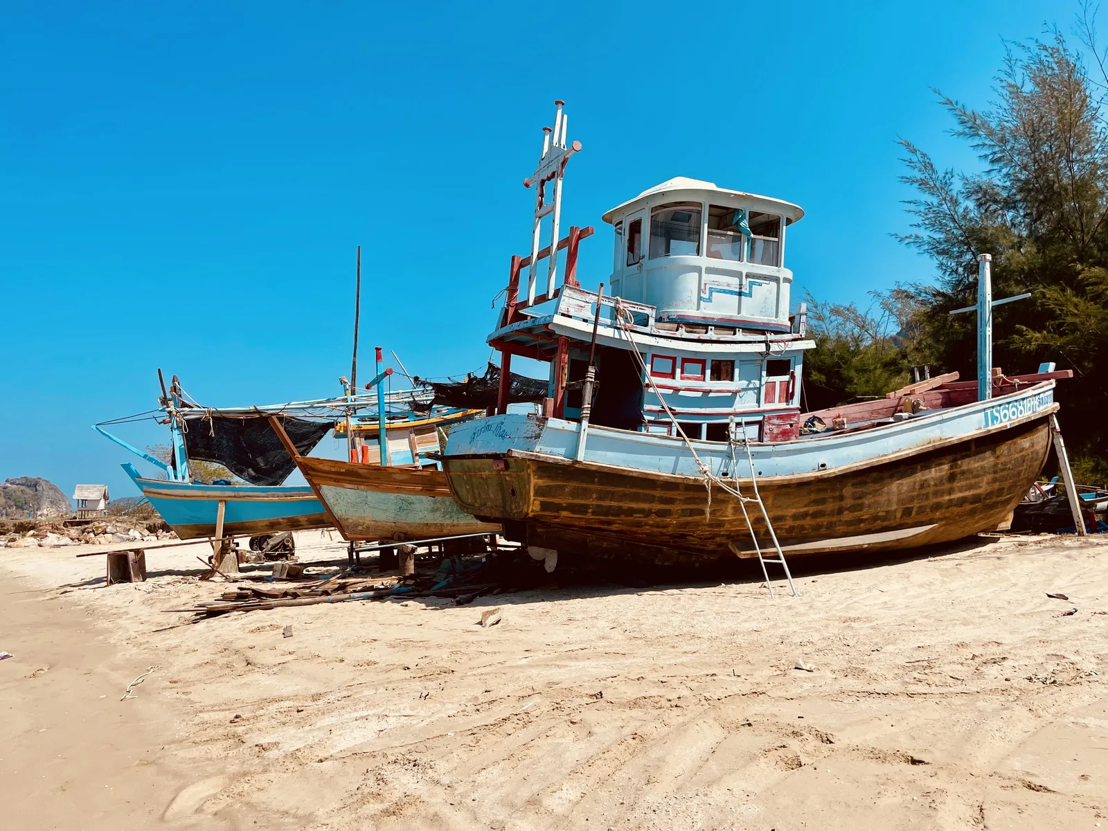 Wooden fishing boats pulled up on the empty sand under a deep blue sky at Dolphin Bay, Sam Roi Yot