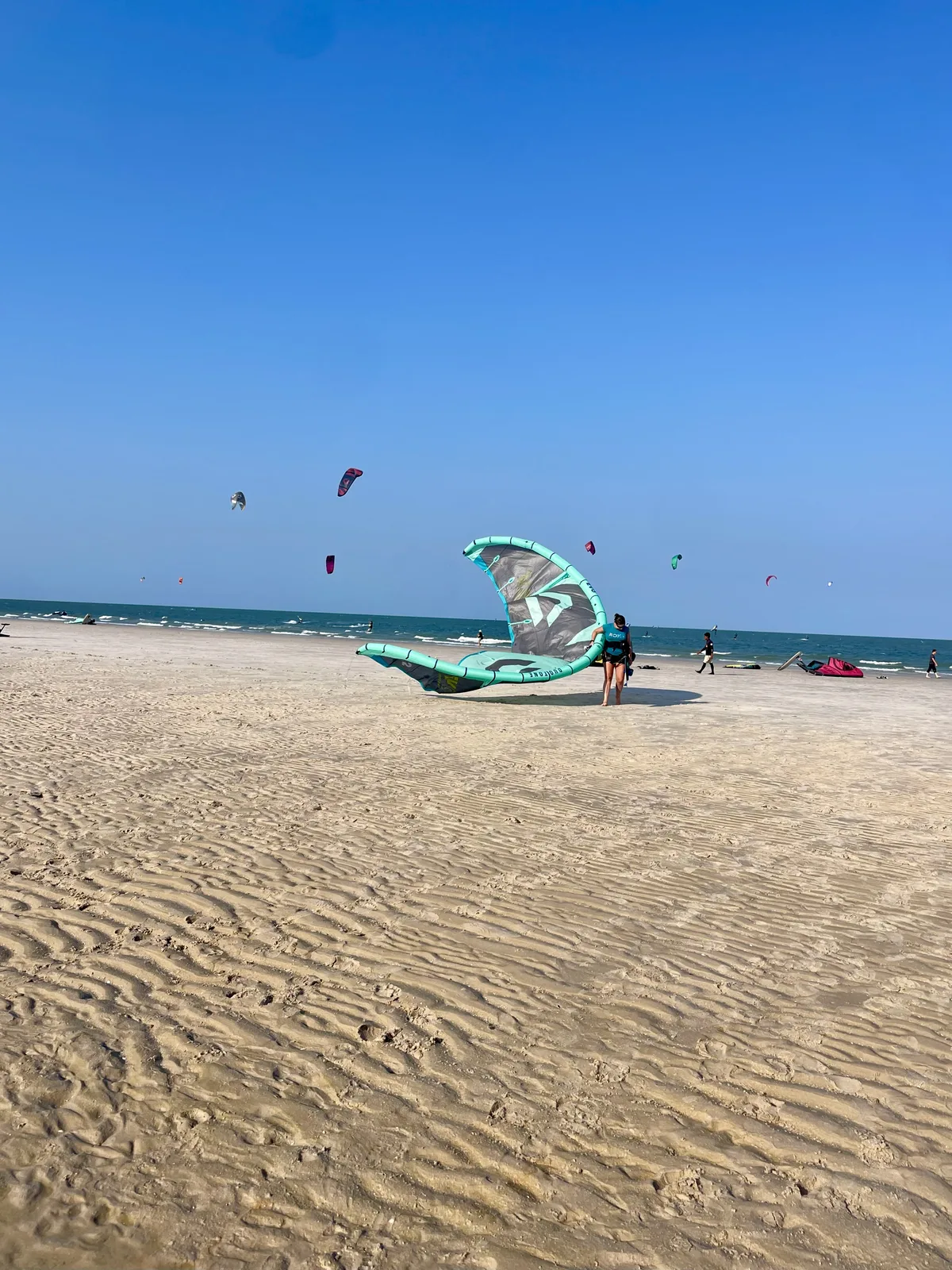 Kitesurfers on the wide sandy beach at Hua Hin, Thailand, with colourful kites flying over the Gulf