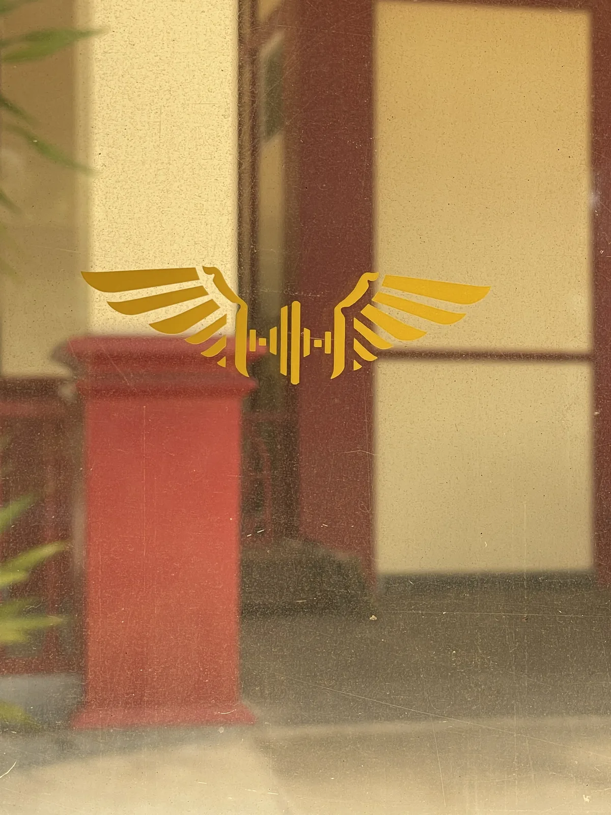 The golden winged garuda emblem of the State Railway of Thailand on a station window, with the red platform pillars behind