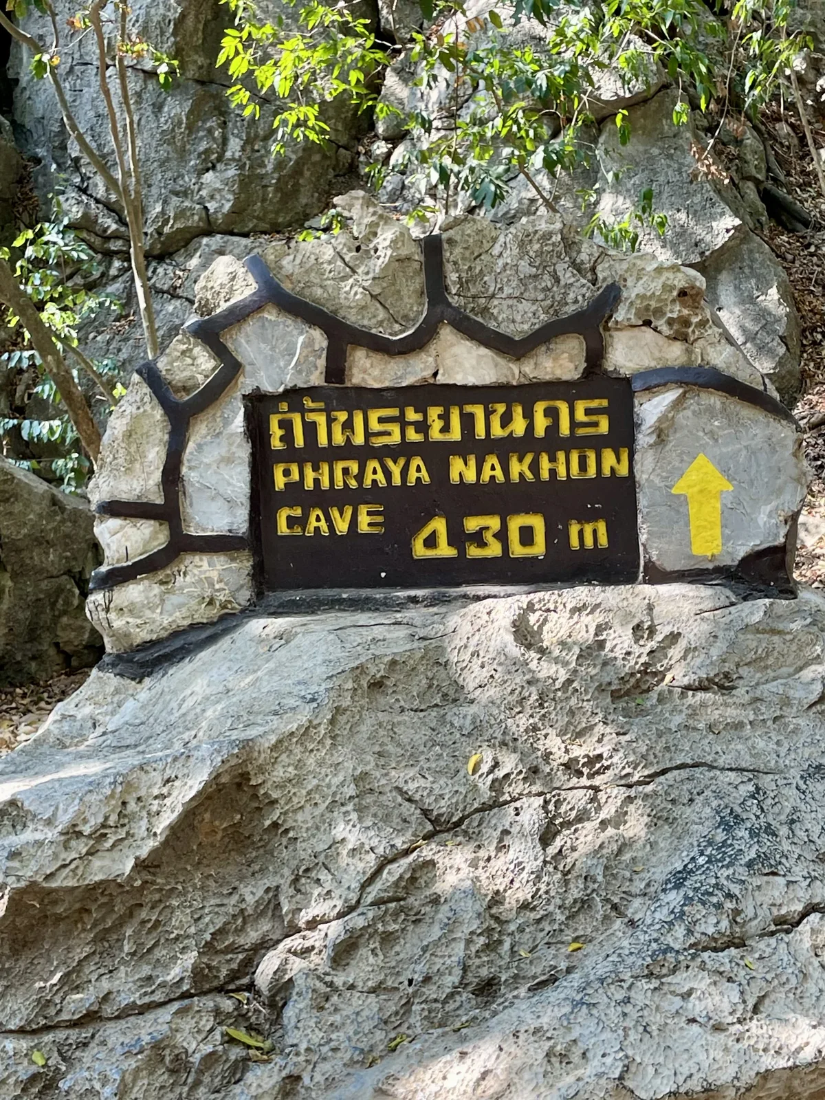 A carved stone trail marker reading Phraya Nakhon Cave 430 m with a yellow arrow pointing uphill