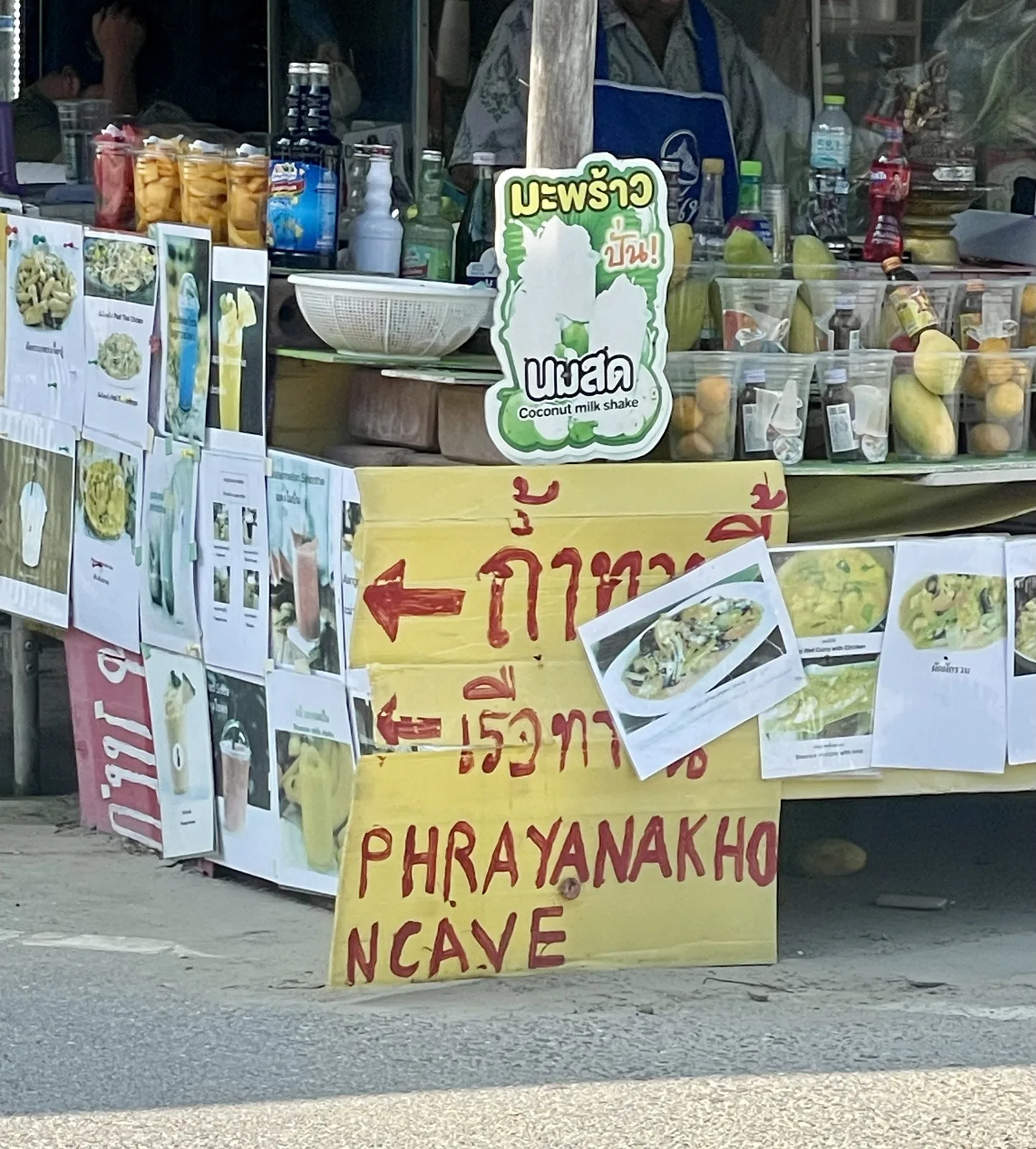 A roadside food and drink stall near Sam Roi Yot with a hand-painted sign pointing to Phraya Nakhon Cave