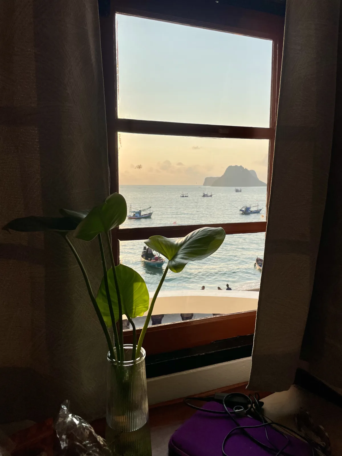 A window with a plant in the foreground, curtains and a view of the ocean and karsts in Prachuap Khiri Khan Thailand